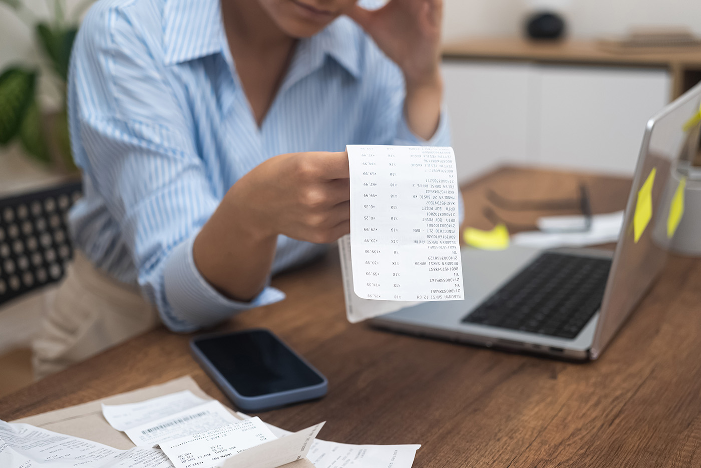 Frustrated woman looks at document with total price of utilities leaning on hand with head